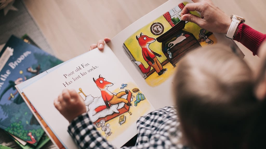 Parent and child reading a book with cartoon foxes.